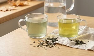 Ket pohar zold tea egymas mellett, csapvizzel es szurt vizzel fozve, mogottuk uvegkancso